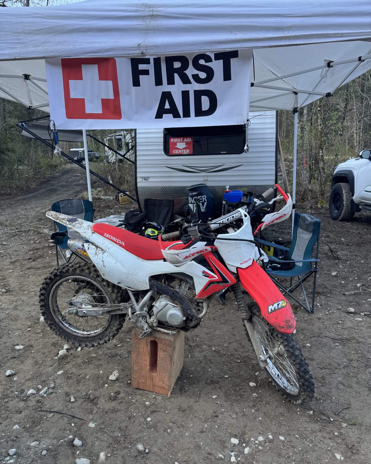 A first aid station set up under a canopy beside a trailer, with dirt bikes parked in front.
