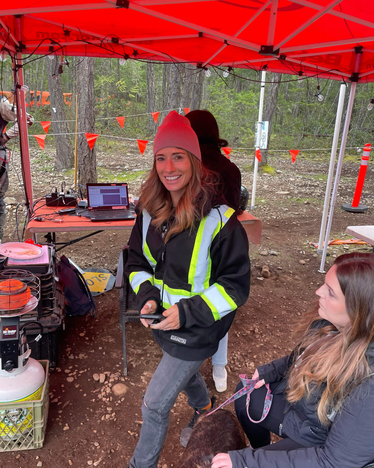 Cait Wolfe in high-visibility outerwear at an event medical station set up under a canopy in the forest.