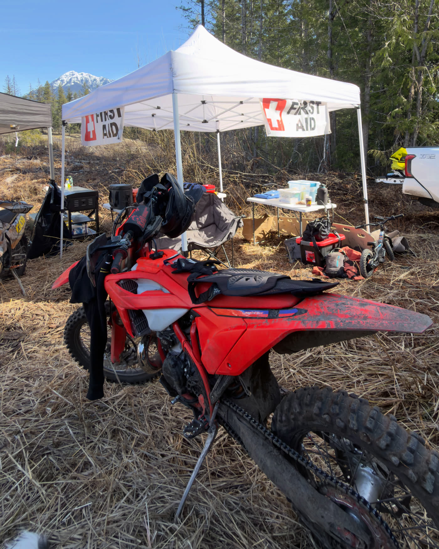 A Wolfe Medical first aid station set up beside a mountain trail, with a dirt bike parked in front and snow-capped peaks behind.